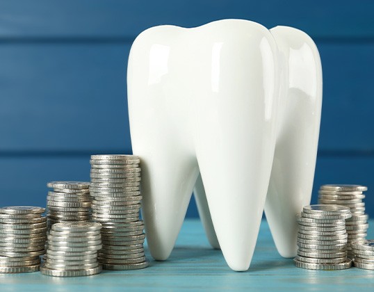 A large, ceramic tooth model and coins on a light blue wooden table