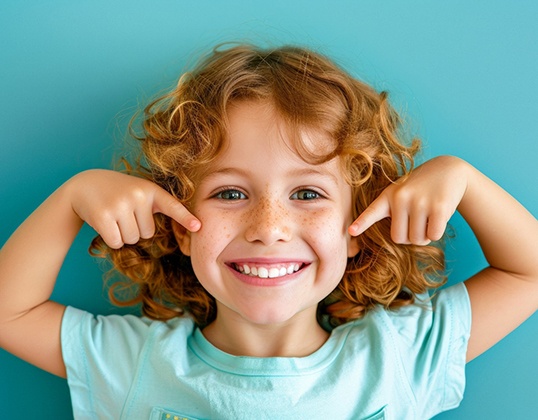 Child with freckles pointing to healthy smile